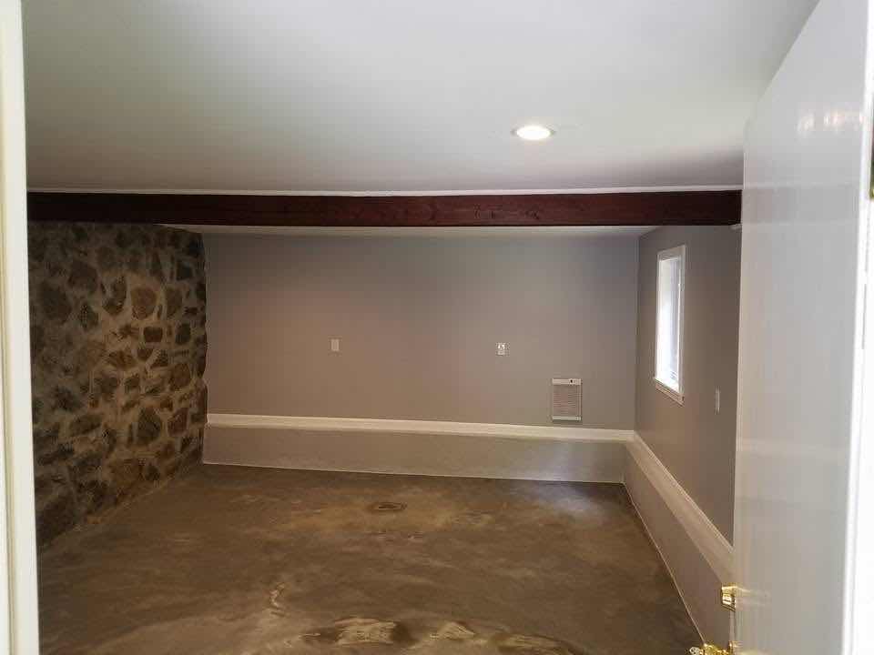 Exposed fieldstone accent wall in a finished basement with a wood beam ceiling, built by Magic Tools Contracting