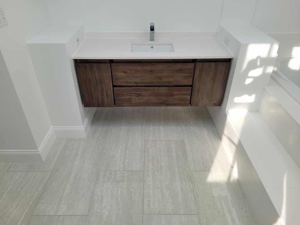Floating wood vanity with a white quartz top on a large-format porcelain tile floor, installed by Magic Tools Contracting