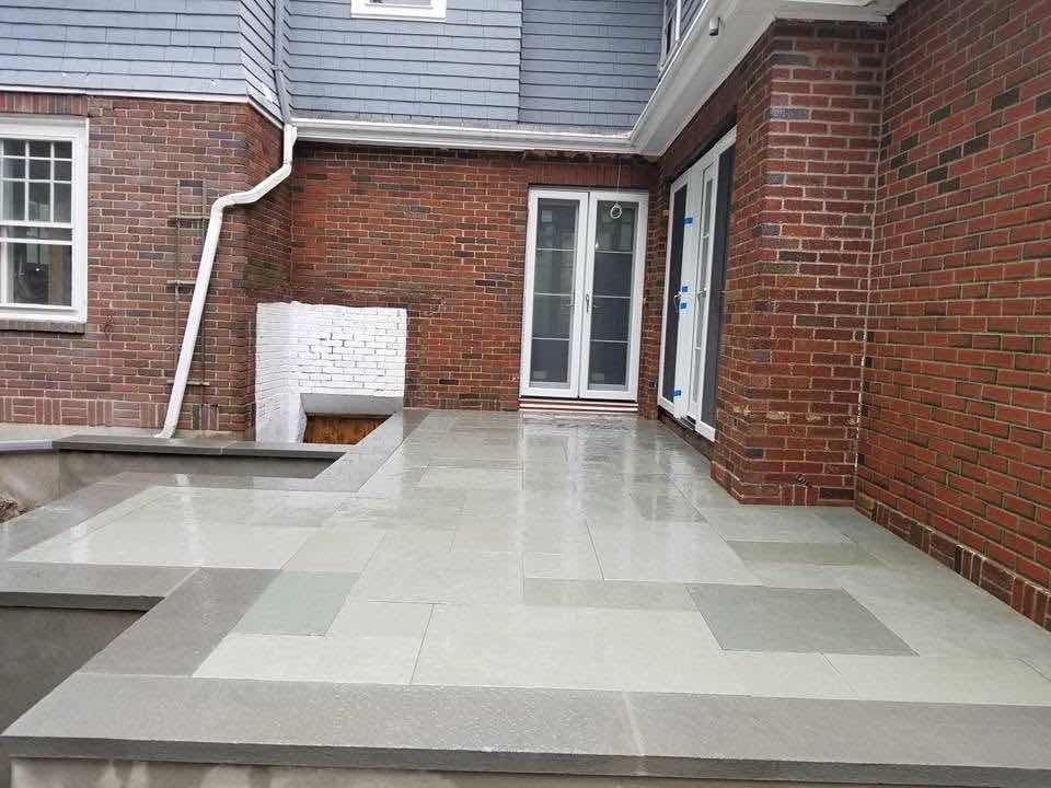 Bluestone paver patio against a brick home with a painted fireplace surround, installed by Magic Tools Contracting