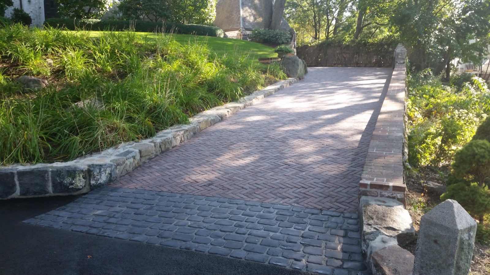 Herringbone brick paver driveway bordered by a stone and brick wall, installed by Magic Tools Contracting