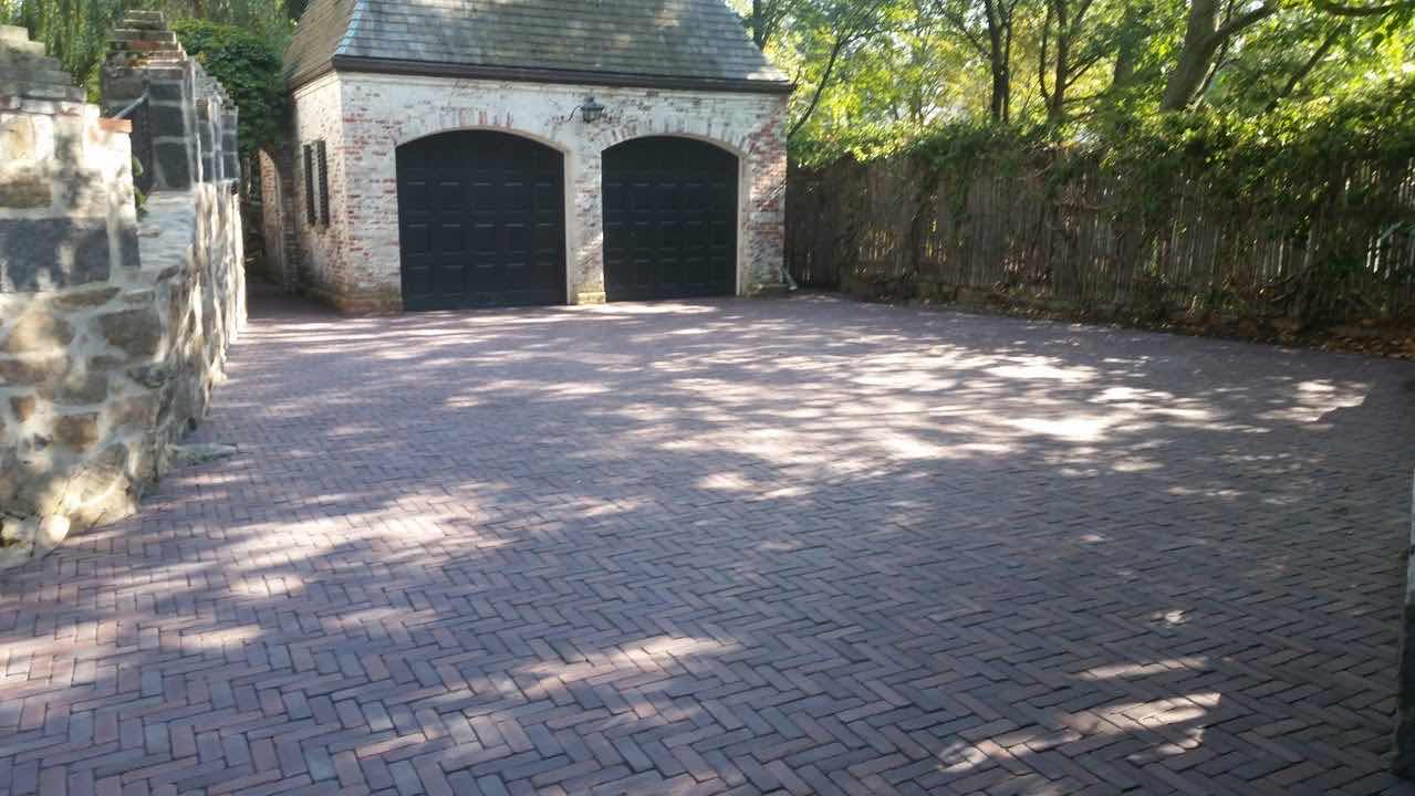Herringbone brick driveway in front of a carriage house with arched garage doors, installed by Magic Tools Contracting