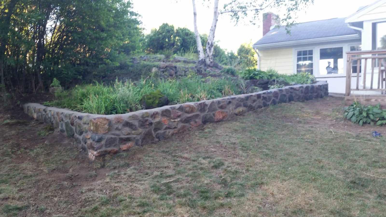 Curved fieldstone retaining wall built along a backyard garden bed by Magic Tools Contracting